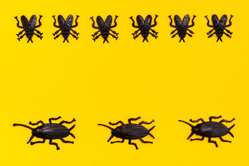 Black plastic cockroaches and black plastic flies on a yellow cardboard background. Ready Halloween illustration. Copy space