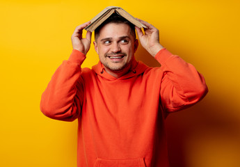 Funny man with book on head on yellow background