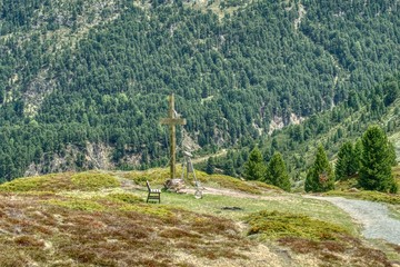 road in the mountains, hiking trail in the Alps, by the path a place for reflection and rest with a bench and a large roadside cross, landscape of alpine forests and meadows