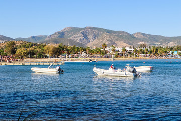 Fototapeta na wymiar Beautiful bay with blue water, sandy beach and boats. Small town and green mountains on the coast of the Aegean sea