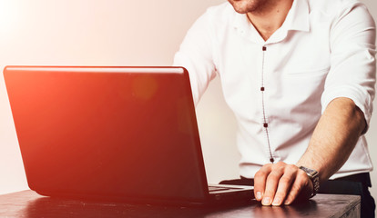 Cropped image of a young man working on his laptop at the table. Rear view of business man hands busy using laptop at office desk, young male typing on computer. Selective focus. Closeup.