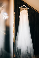 A wedding dress hangs on a hanger and is mirrored in the glass
