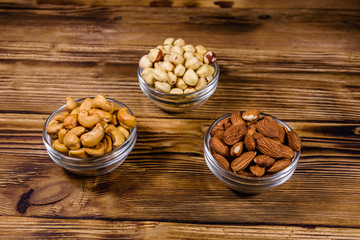 Various nuts (almond, cashew, hazelnut) in glass bowls on a wooden table. Vegetarian meal. Healthy eating concept