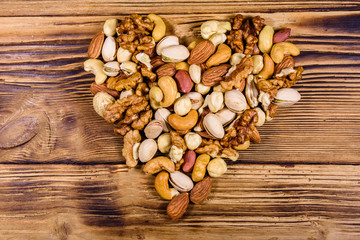Various nuts (almond, cashew, hazelnut, pistachio, walnut) in shape of heart on a wooden table. Vegetarian meal. Healthy eating concept