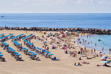 Vacationers people sunbathing on sandy beach of Playa de los Cristianos, enjoy warm Atlantic Ocean waters, Tenerife, Canary Islands, Spain