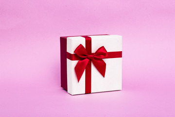 New Year's white gift with a red ribbon and bow on a pink background.