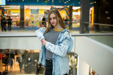 Teenager. Young pretty white caucasian teenage girl with long hair with problem skin and long hair in a shopping center near the railing.
