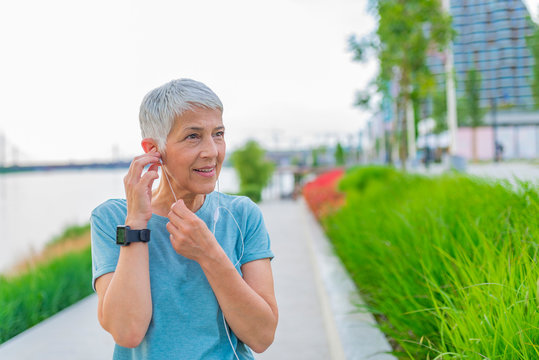 Portrait of smiling senior woman relaxing after exercising. Portrait of senior woman adjusting earphones before exercising. fitness, sport and healthy lifestyle concept - senior woman with earphones