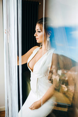 Sexy girl in a white dress with a deep neckline. Portrait with reflection in the window.