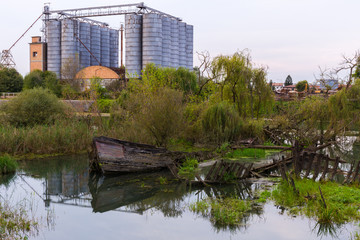 Historical cemetery of sunken wooden shipwrecks in the water in the river with an abandoned factory with silos in the background.