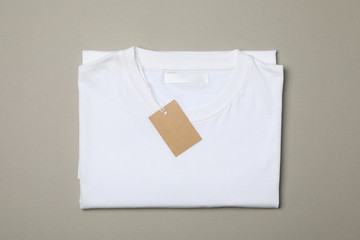 Folded blank white t-shirt with tag on gray background, space for text