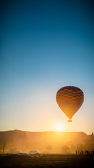 Big colorful air balloon flying against the rising sun over beautiful landscape in Cappadocia, Turkey.  