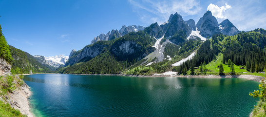 Famous Lake Gosau and Gosaukamm with Mount Dachstein. Spring is here! The snow is melting and spring brings the luscious green back to nature. The sun is about to hide behind the high peaks. - obrazy, fototapety, plakaty