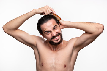 Fototapeta premium Stylish handsome bearded with mustaches have problems combing his hair standning bare isolated over white background. Concept of morning treatment.
