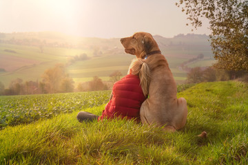 Beste Freunde - ein Kind lehnt sich an seinen Hund, einen Broholmer, an und beide genießen in der Natur den Sonnenuntergang an einem Herbsttag - 299193162