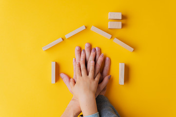 Hands of a father, mother and child one on top of the other placed in a house shape made of wooden...