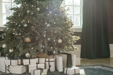 Brightly lit christmas tree with lots of gifts near window