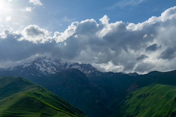 Obraz na płótnie Canvas Landscape mountain view peaks in snow and green hills, deep blue sky and huge white clouds background, Caucasian mountains, Kazbek mountain