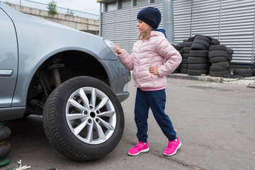Fototapeta na wymiar Little girl at a car service. Replacing wheels on a car. Repair service.