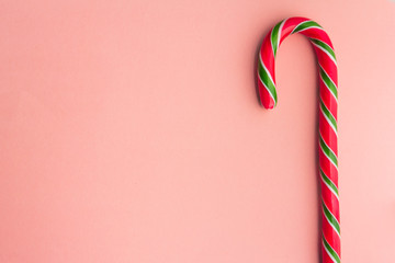 Traditional christmas caramel candy cane on a pink background. Winter Holiday festive greeting card with copy space for the text. Xmas flat lay concept.