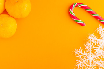 Traditional christmas caramel candy cane, mandarins and snowflakes on a orange background. Winter Holiday festive greeting card with copy space for the text. Xmas flat lay concept.