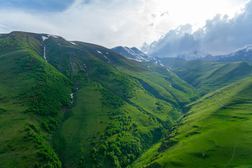 Naklejka premium Landscape mountain view peaks in snow and green hills, deep blue sky and huge white clouds background, Caucasian mountains, Kazbek mountain