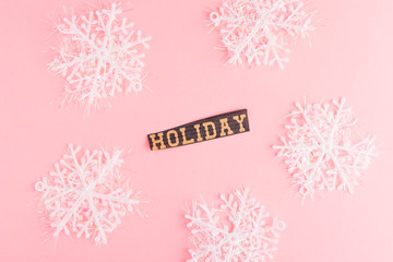 Snowflakes on a pink background with Holiday lettering inscription. Winter Holiday festive greeting gift card. Xmas flat lay concept.