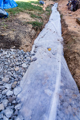 Fabric covers drainage rock and pipe to keep a French drain clear of debris in this DIY home...