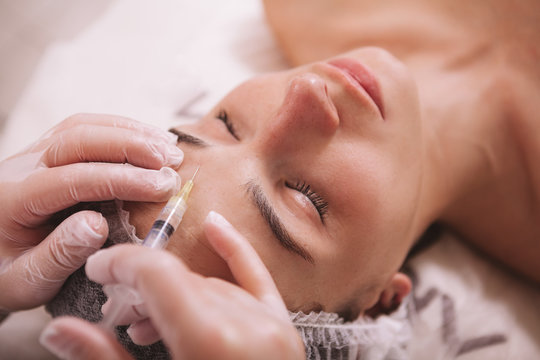 Top view close up of a woman receiving filler injections in forehead. Professional cosmetologist injecting hyaluronic acid into skin of female client