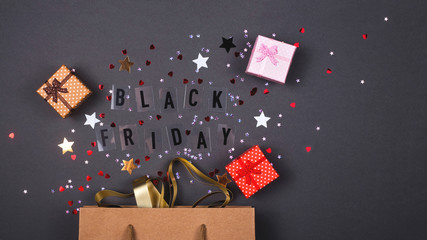 Kraft paper bag on bright dark background. With gift boxes and confetti. Black friday is written.