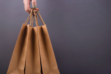Kraft paper bags in woman's hands on bright dark background. Minimal Black friday christmas gift...