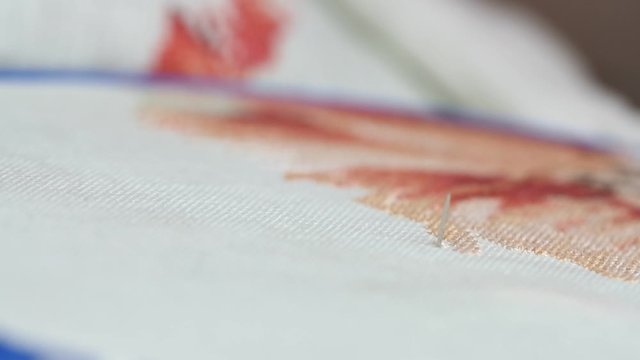 Woman hands doing cross-stitch of red flower. A close up of embroidery.