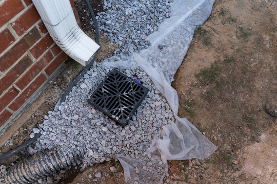 Plastic catch basin installed under a downspout to alleviate drainage issues against a red brick home