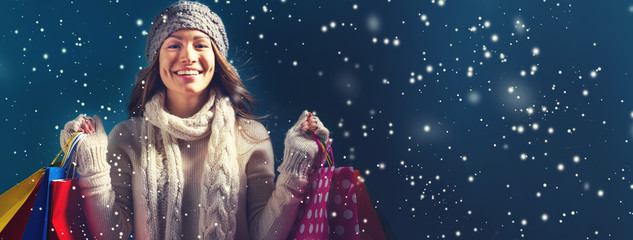 Happy young woman holding shopping bags in a snowy night