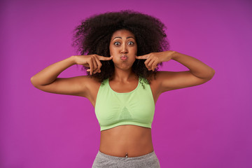 Obraz premium young curly dark skinned female woman lady casual hairstyle wearing light green top casual clothes isolated standing posing purple background looking at camera
