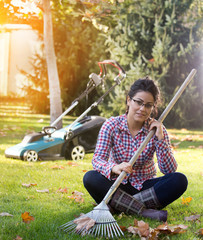 Woman holding rake for leaves and resting on lawn