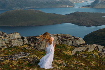 Fototapeta premium Back of girl in wedding dress in mountains looking to fjord