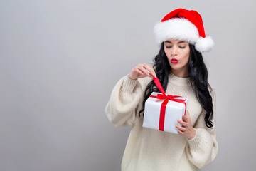 Young woman with santa hat holding a gift box on a gray background