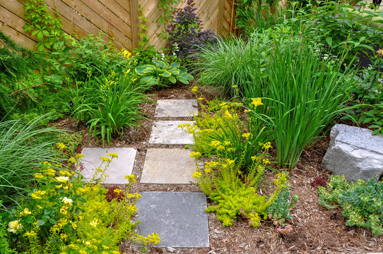 Detail of an easy care garden featuring natural stone flagstone path, perennial planting, and privacy fencing.