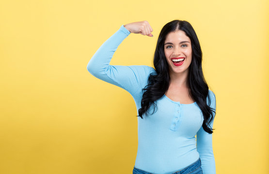 Powerful young woman in a success pose on a yellow background