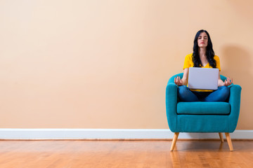Young woman with laptop in a meditation pose pose sitting in a chair