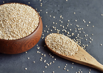 Quinoa in a brown wooden bowl and spoon on dark stone background. Dry uncooked cereal grains, cooking ingredient