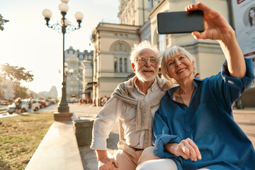 Happy moments. Cheerful senior couple in casual clothes making a selfie while sitting on the bench together