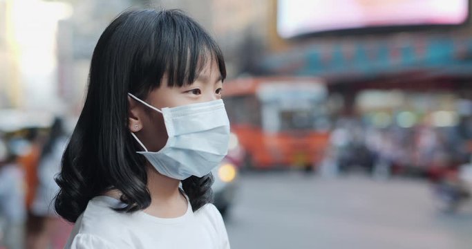 Little girl wearing mask and looking to camera at city. Health care and medical concept.
