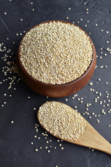Uncooked quinoa in a brown wooden bowl and spoon on dark stone background. Dry cereal grains, cooking ingredient