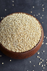 Organic dry quinoa cereal grains in wooden bowl on black stone background. Cooking ingredient.