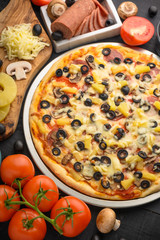 Italian pizza with ingredients on a dark background. Vertical photo.