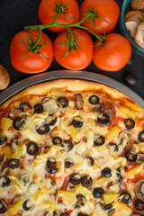 Italian pizza with ingredients on a dark background. Vertical photo.