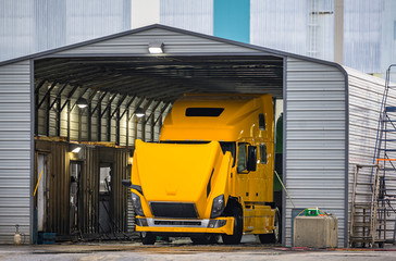 Naklejka premium Big rig bright yellow semi truck with open hood washes in a trucks car wash in an industrial zone