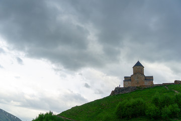 Gergeti Trinity Church also known as Tsminda Sameba on the background of a mountain ridge and clouds, Stepantsminda, Kazbegi